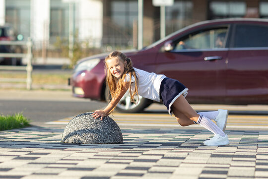 Happy funny school little girl pushing stone hard or doing outdoor exercises. Sport lifestyle. Impossible concept.