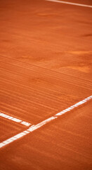 Close-up of reddish-brown clay tennis court surface, showing texture and white lines, representing sport, competition, and energy