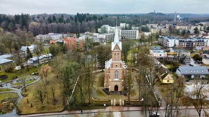 Aerial view of Birstonas medical SPA resort, Lithuania. Aerial view of a quaint town featuring a prominent Gothic-style church with a tall spire at its center, nestled among trees. 