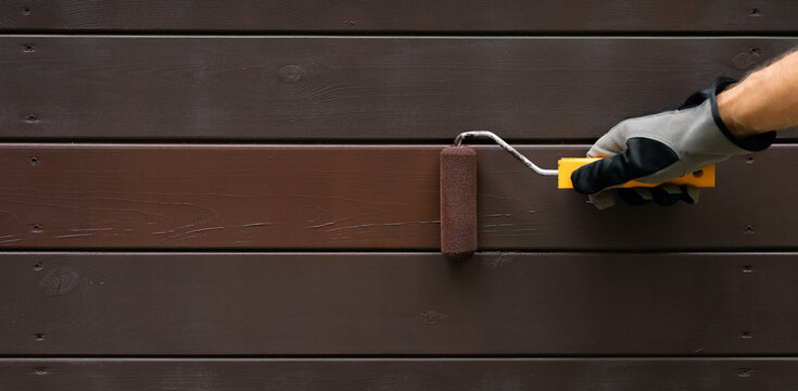 hand with paint roller painting wooden house exterior siding with protective color. wood protection. banner with copy space