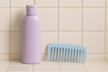 Purple shampoo bottle and blue comb on tiled surface, showcasing hair care essentials