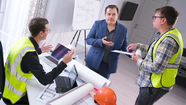 The chief engineer and his assistant ask the boss for a raise. Three men are talking in the architect's office, two of them wearing green signal vests