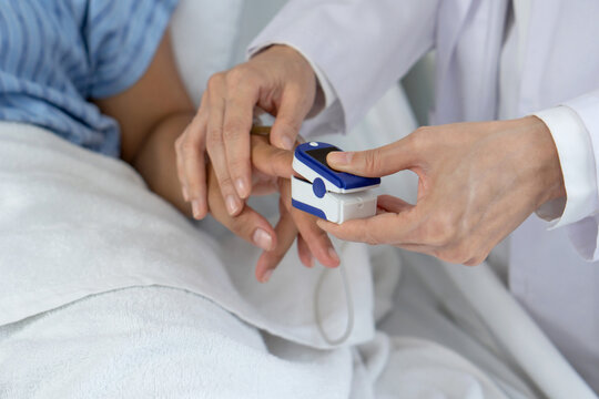 A healthcare professional is using a fingertip pulse oximeter on a patient’s finger in a hospital room. This procedure is crucial for assessing respiratory health and blood oxygen level. Close up
