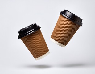 two brown takeaway coffee cups with dark lids and blank labels floating isolated on white background