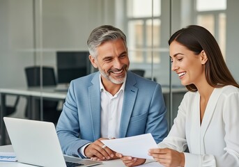 Obraz premium Smiling colleagues collaborating on a document at a modern office desk with a laptop and natural light