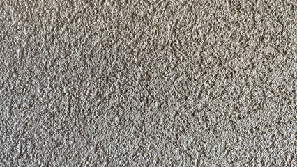Horizontal background of rough textured beige plaster wall with grainy stucco finish and natural irregular pattern
