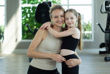Smiling mother and daughter embracing in a bright gym during a fun workout session