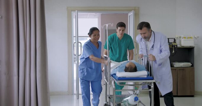 asian female nurse and two male doctors pushing stretcher with unconscious patient into hospital room while preparing for immediate critical care treatment and trauma intervention during emergency