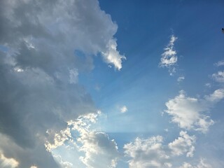 Sun Rays Breaking Through Dramatic Cloudscape. Sunlight beams pierce through scattered clouds in a vivid blue sky, creating a dramatic and peaceful natural sky scene