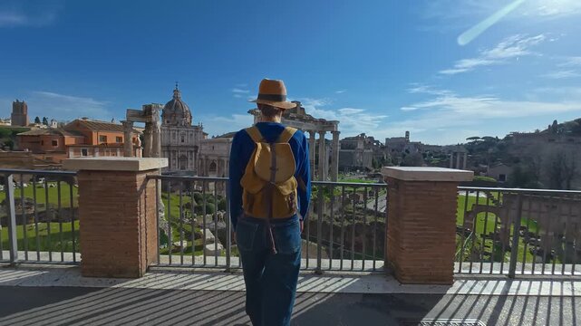 Tourist woman in a hat and with a backpack is considering the sights Columns of ancient Rome at the Roman Forum. Italy. View of a walking girl from the back against the backdrop of landmarks