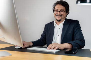 Fototapeta premium A cheerful male office employee working at his desk in a modern office environment, representing productivity and job satisfaction.