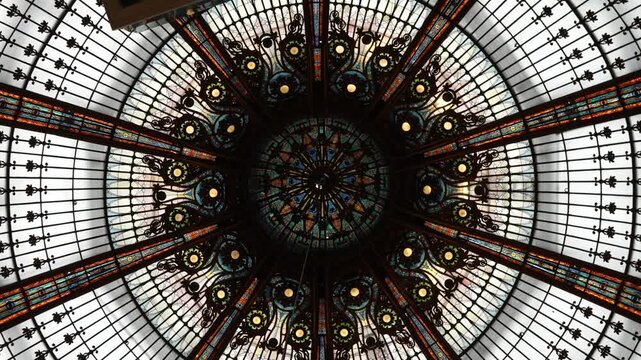 Intricate stained glass dome with ornate ironwork inside Galeries Lafayette under natural daylight
