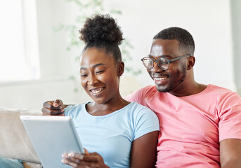 Portrait of a lovely young couple together holding a tablet on sofa at home