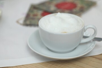 White coffee cup with foam on top sits on a white saucer