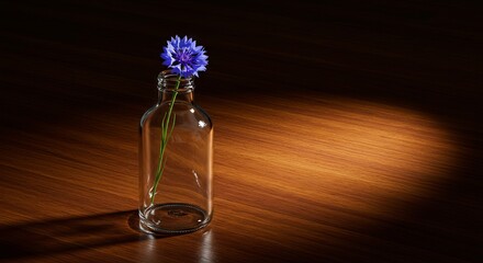 Single blue flower in clear glass bottle on wooden surface