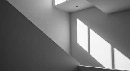 Obraz premium Sunlight from a high window casting sharp diagonal shadows across the stark white walls of a modern architectural interior.