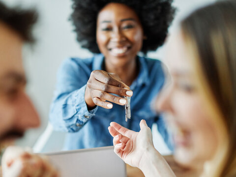Portrait  of real estate agent or youn businesswoman giving keys to couple of customers in office