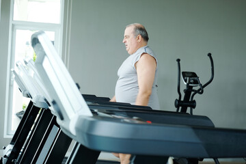 An overweight man running on a treadmill while exercising at the gym.