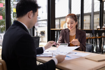 Asian businesswoman and businessman are holding paper documents financial analysis data charts in office working space.