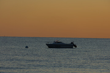 Obraz premium A small white motorboat with a light-colored canvas cover floats serenely on the calm blue water under a pale, muted sky.