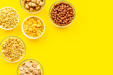 Various corn cereals in bowls on yellow background top view copyspace