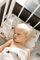 small cute blonde child sleeping in his white crib on special pillow