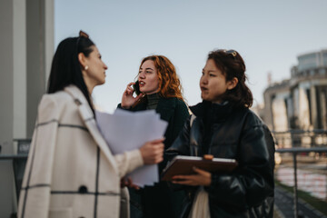 Three young professionals engage in a discussion outdoors, showcasing teamwork, communication, and strategic planning in business while interacting with notes, technology, and a clipboard under