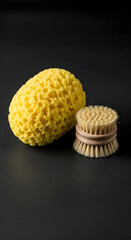 Natural sea sponge and wooden dish brush on a dark surface, minimalist cleaning tools