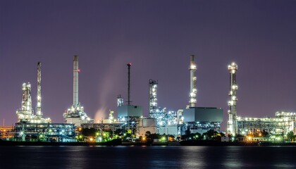 Fototapeta premium Industrial oil refinery plant glowing at twilight with water reflections
