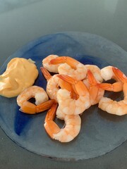 Closeup image of prawns served with cocktail sauce on a round glass plate
