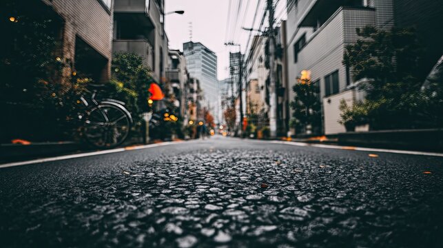 Urban street perspective, focusing on asphalt texture. City buildings and foliage visible in the background