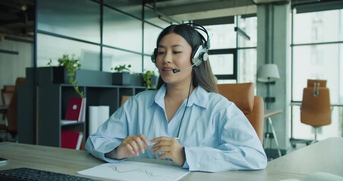 A focused young woman, who is wearing a headset, is deeply engaged in her work at a modern contemporary office setup