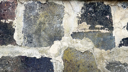 Rough stone wall showcases an array of dark and light hues with visible moss and lichen growth