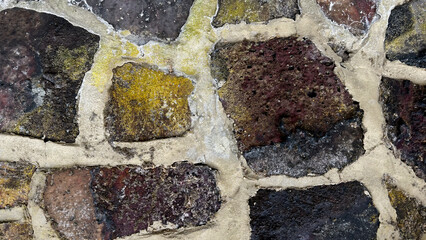 Fototapeta premium The wall displays a variety of stones in different colors and textures, showcasing natural weathering. Sunlight highlights the unique patterns and shapes of each stone piece
