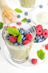 Healthy breakfast chia pudding with with matcha latte tea and fresh summer berries in glasses, white background copy space