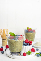 Healthy breakfast chia pudding with with matcha latte tea and fresh summer berries in glasses, white background copy space
