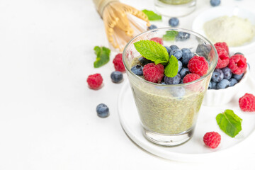 Healthy breakfast chia pudding with with matcha latte tea and fresh summer berries in glasses, white background copy space
