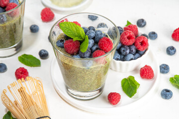 Healthy breakfast chia pudding with with matcha latte tea and fresh summer berries in glasses, white background copy space