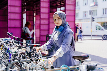 Muslim woman unlocking bicycle in city center near purple structure