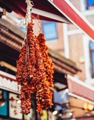 Strings of dried red peppers hanging in a traditional outdoor market under a red canopy, symbolizing natural food preservation and cultural culinary heritage.