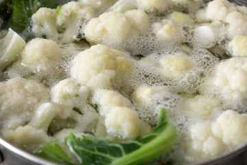 Fresh cauliflower is boiled in a saucepan with water. The vegetable is divided into florets and boiled in a saucepan.