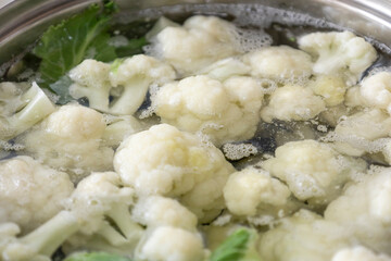Fresh cauliflower is boiled in a saucepan with water. The vegetable is divided into florets and boiled in a saucepan.