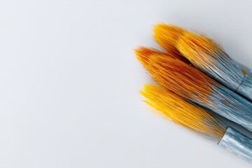 Fototapeta premium Three Paint Brushes with Bright Orange Bristles on a Minimalist Background for Artistic Creations