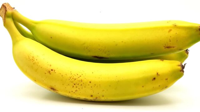 Time lapse video of bananas ripening on a white background, from green to ripe yellow with brown spots.