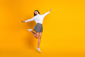 Obraz premium Dynamic young woman posing with joy in white shirt and skirt against a vibrant yellow background