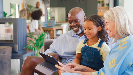Grandparents And Granddaughter Sitting On Sofa With Digital Tablet At Home