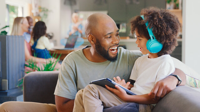 Father And Son Using Digital Tablet At Home With Multi-Generation Family In Background