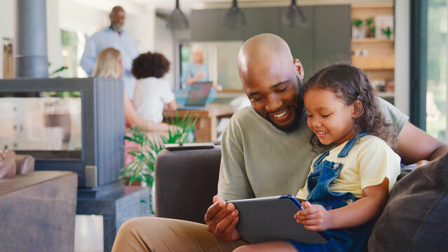 Father And Daughter Using Digital Tablet At Home With Multi-Generation Family In Background