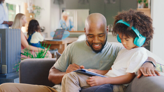 Father And Son Using Digital Tablet At Home With Multi-Generation Family In Background