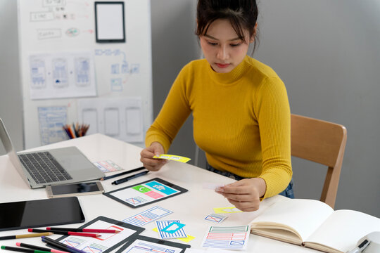 Asian adult woman designer creating user experience interface design wireframes prototyping mobile web application at professional office studio workspace
